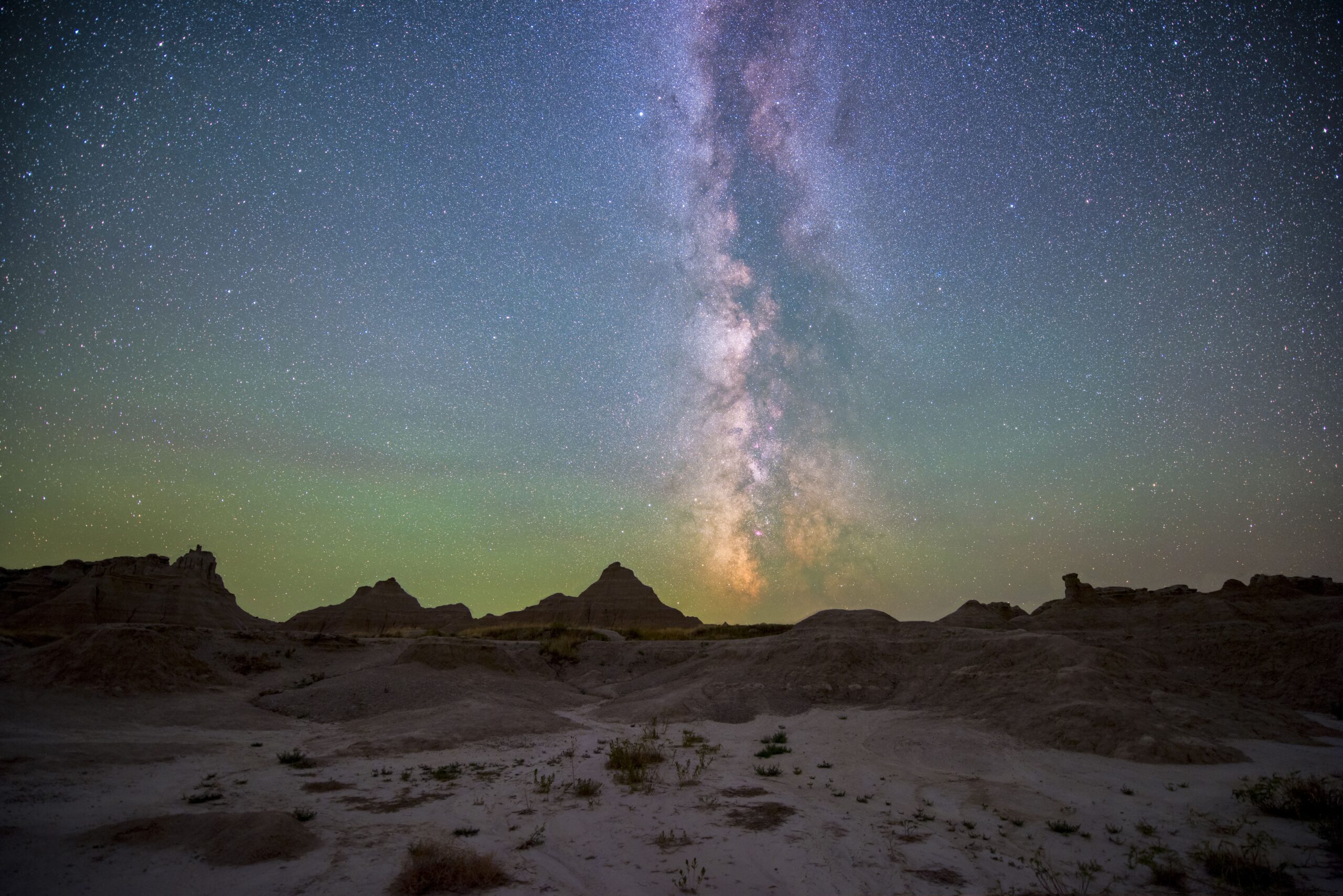 Star-filled Milky Way rising over eroded Badlands formations and sparse scrub brush under a clear night sky