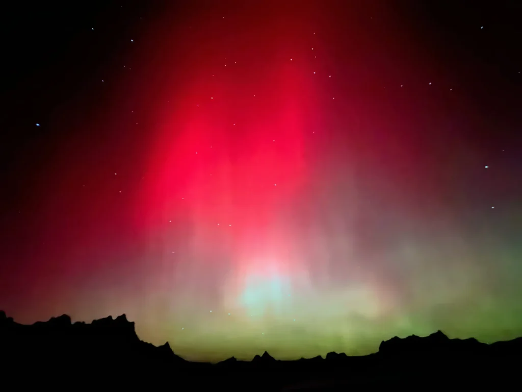 THE BEST STARGAZING SPOTS IN BADLANDS NATIONAL PARK — A DARK SKY PARK GUIDE 3 Red and green aurora over the silhouetted formations of badlands national park at night